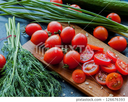 Fresh red cherry tomatoes with herbs and leek sprinkled with sea salt on the wooden board on the table, top view of vegetables covered with drops. 126676393
