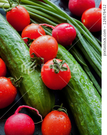 Fresh red cherry tomatoes, green leek, radish and cucumber on the black table background, top view of vegetables covered with water drops. 126676412