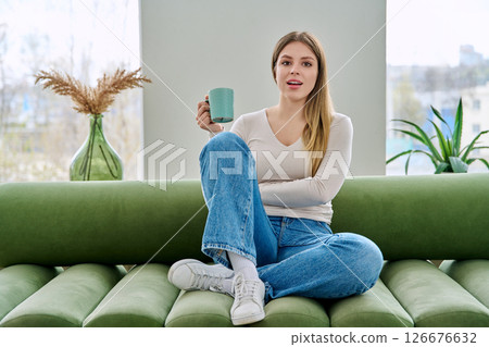 Portrait of relaxed beautiful young woman sitting at home on sofa with cup 126676632