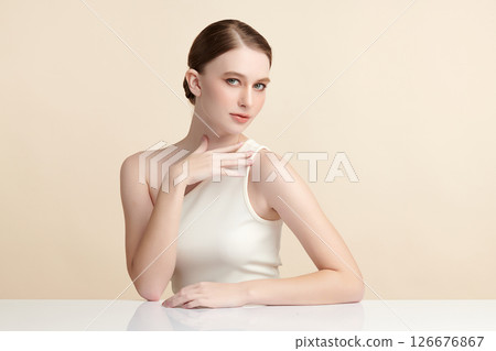 A beautiful young woman with clean, fresh skin against a beige background. Skincare, facial treatment, cosmetology, beauty, and spa. An elegant portrait of an woman. 126676867