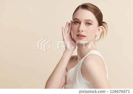 A beautiful young woman with clean, fresh skin against a beige background. Skincare, facial treatment, cosmetology, beauty, and spa. An elegant portrait of an woman. 126676871