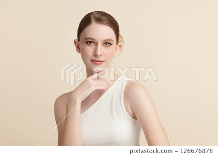 A beautiful young woman with clean, fresh skin against a beige background. Skincare, facial treatment, cosmetology, beauty, and spa. An elegant portrait of an woman. 126676878