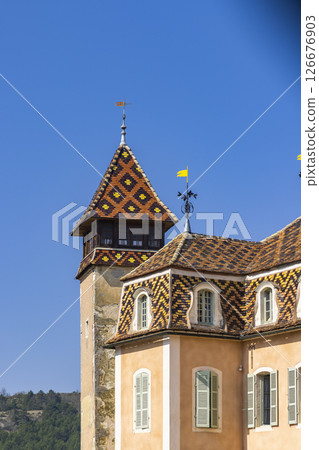 Colorful glazed tile roof and tower of Chateau de Monthelie in Burgundy, France, shining under blue sky 126676903