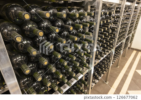 Wine bottles aging on metal shelves in cellar with tiled floor 126677062
