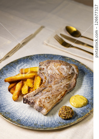 Grilled pork chop served with french fries and mustard on elegant blue plate Grilled pork chop served with french fries and mustard on elegant blue plate 126677317