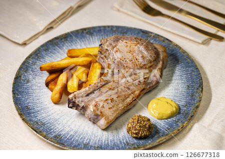 Grilled pork chop served with french fries and mustard on elegant blue plate Grilled pork chop served with french fries and mustard on elegant blue plate 126677318