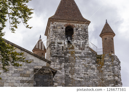 Church bell tower with conical roofs in Auvillar, France, showing stone walls and cloudy sky 126677381