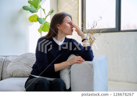 Serious middle-aged woman looking out the window, sitting at home on sofa 126678267