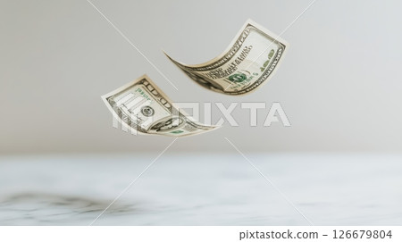 Two one hundred dollar bills are slowly falling onto a white marble surface, depicting concepts of wealth, investment, and financial transactions 126679804