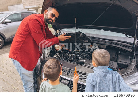 Father and sons repairing car together with the hood open. A heartfelt moment of bonding, fatherhood, parenting, teamwork, and learning. Celebrating Father Day through shared hands-on experience. 126679980