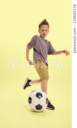Boy stopping soccer ball with foot in full concentration, mid-action pose against yellow floor, close-up on movement, symbol of sport and childhood activity Boy stopping soccer ball with foot in full concentration, mid-action pose against yellow floor, close-up on movement, symbol of sport and childhood activity 126680138