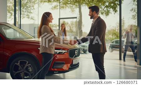 Salesman and customer shaking hands in a vibrant car dealership showroom, celebrating the successful purchase of a striking new red car, finalizing the agreement with satisfaction 126680371