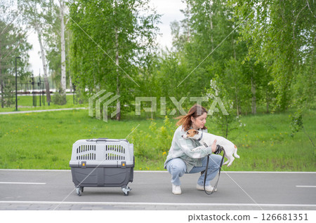 Owner walks Jack Russell Terrier and carries cage for safe travel. 126681351