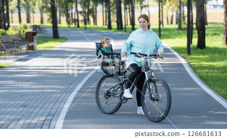 Caucasian woman riding a bicycle with her toddler son sitting behind her in a child seat. Caucasian woman riding a bicycle with her toddler son sitting behind her in a child seat. 126681633