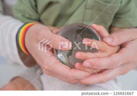 A faceless woman with a rainbow headband and her son hold a glass globe.  126681667