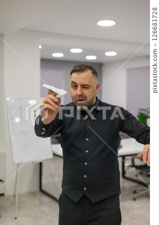 Caucasian bearded man launching paper airplane in office.  126681728