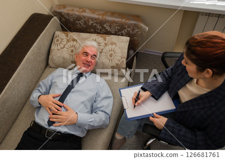 An elderly man lies on a couch during an appointment with a psychotherapist. An elderly male patient in an individual consultation with a female psychologist An elderly man lies on a couch during an appointment with a psychotherapist. An elderly male patient in an individual consultation with a female psychologist 126681761