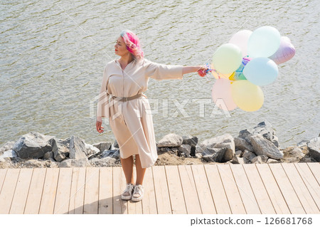 A woman with colored hair and an armful of balloons walks along the river embankment. A woman with colored hair and an armful of balloons walks along the river embankment. 126681768