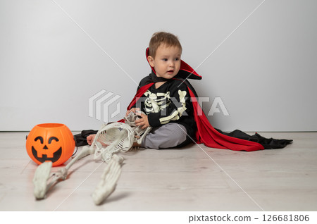 Little Caucasian boy in Dracula costume holding skull on white background.  126681806