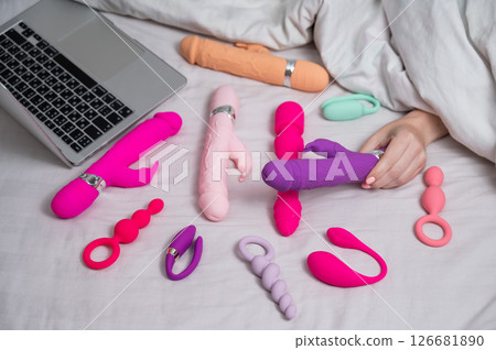 Woman holding sex toy. Various vibrators and laptop on bed. Woman holding sex toy. Various vibrators and laptop on bed. 126681890
