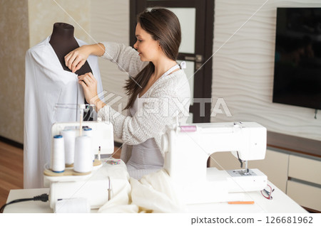 Caucasian woman sews a dress at home. Workspace of a seamstress 126681962