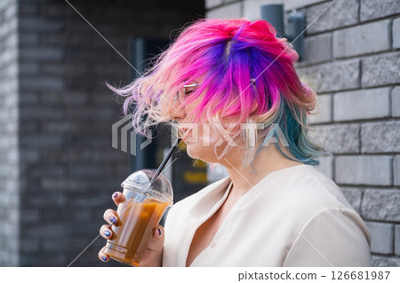 Close-up portrait of Caucasian woman with multi-colored hair wearing glasses. The hairstyle model is drinking a cold drink. 126681987