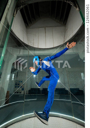 A man in overalls and a protective helmet enjoys flying in a wind tunnel. Free fall simulator A man in overalls and a protective helmet enjoys flying in a wind tunnel. Free fall simulator 126682061