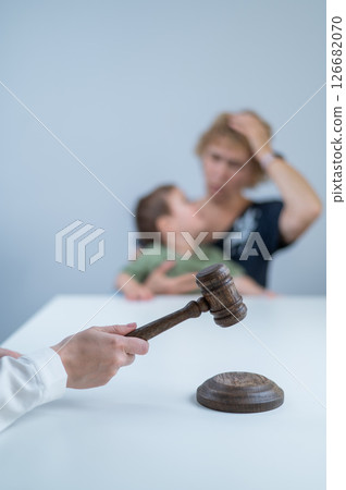A judge hits a gavel against the backdrop of an elderly woman holding a child.  126682070