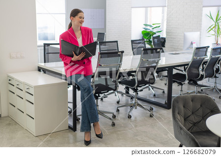 Smiling business woman in pink jacket reading documents in office.  126682079
