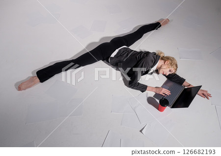 A ballerina dressed in a business suit sits in a middle twine, works at a laptop and drinks coffee. Flexible woman works at the computer A ballerina dressed in a business suit sits in a middle twine, works at a laptop and drinks coffee. Flexible woman works at the computer 126682193