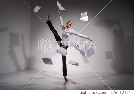 A graceful ballerina in a business suit throws documents. Business woman dance barefoot on a white background A graceful ballerina in a business suit throws documents. Business woman dance barefoot on a white background 126682195