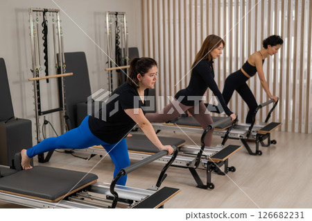 Three Asian women doing Pilates on a reformer.  126682231