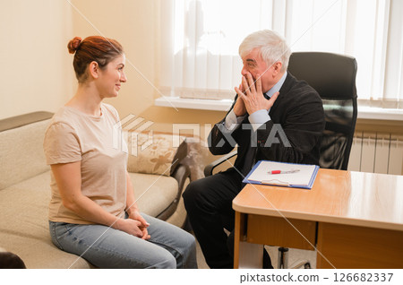 Mature gray-haired male psychotherapist in session with female patient. Smiling caucasian woman at a psychologist appointment. 126682337