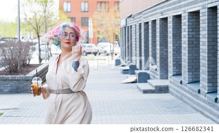 Close-up portrait of curly Caucasian woman with multi-colored hair wearing glasses. The hairstyle model is drinking a cold drink 126682341