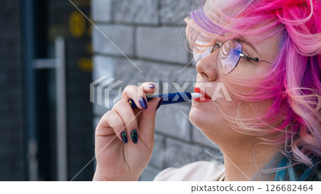 Caucasian woman with colored hair smokes an electronic cigarette. 126682464