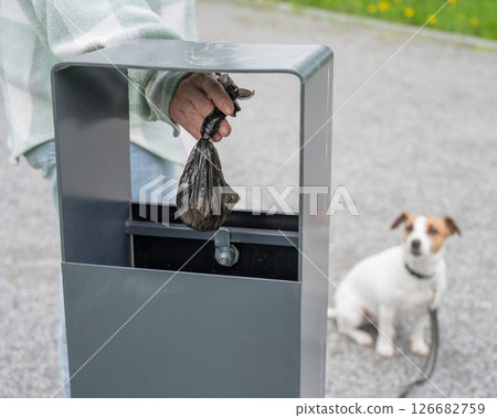 Responsible Dog Owner Disposing of Waste in Park Bin.  126682759