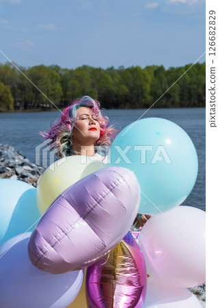 A woman with colored hair with an armful of balloons against a blue sky. A woman with colored hair with an armful of balloons against a blue sky. 126682829