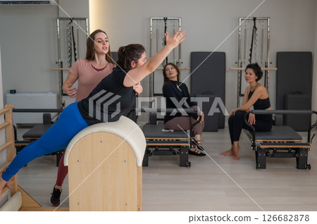 Three women doing Pilates on a reformer and a Pilates barrel.  126682878