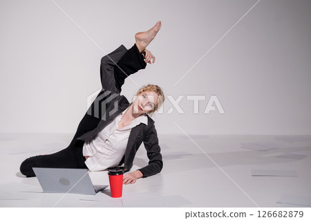 Barefoot ballerina dressed in a business suit poses for a laptop and drinks coffee. Flexible woman works at the computer 126682879