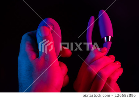 Woman holds curved vibrator while man holds remote control in neon light.  126682896
