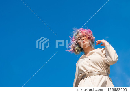 A woman with colored hair walks outdoors. Portrait of a girl against the blue sky.  126682903