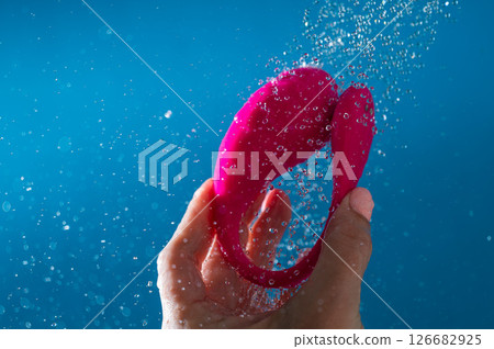 Woman washing pink curved vibrator in shower. Waterproof sex toy on blue background. 126682925
