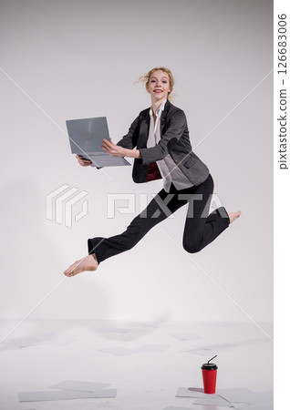 Barefoot ballerina in business suit jumping with laptop on white background.  126683006
