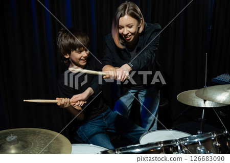 Young caucasian woman teaches a boy to play the drums in the studio on a black background. Music school student Young caucasian woman teaches a boy to play the drums in the studio on a black background. Music school student 126683090