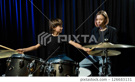 Young caucasian woman teaches a boy to play the drums in the studio on a black background. Music school student Young caucasian woman teaches a boy to play the drums in the studio on a black background. Music school student 126683131