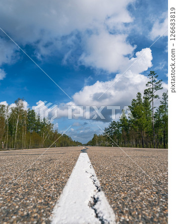 Wide open road stretches through a forest under a blue sky with fluffy clouds on a clear sunny day Wide open road stretches through a forest under a blue sky with fluffy clouds on a clear sunny day 126683819