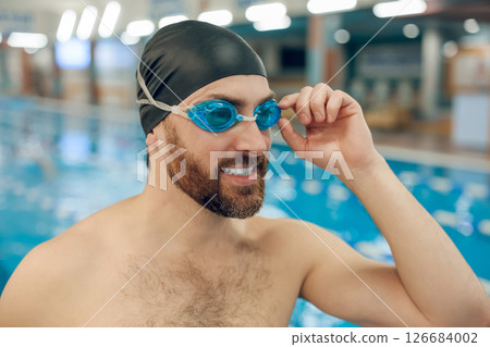 Well-built young man in swimming cap in the pool looking contented Well-built young man in swimming cap in the pool looking contented 126684002