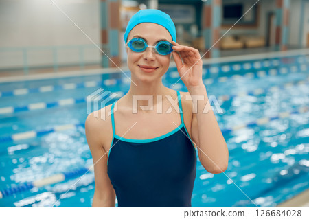 Young woman in swimsuit and swimming cap getting ready to swim in the pool Young woman in swimsuit and swimming cap getting ready to swim in the pool 126684028