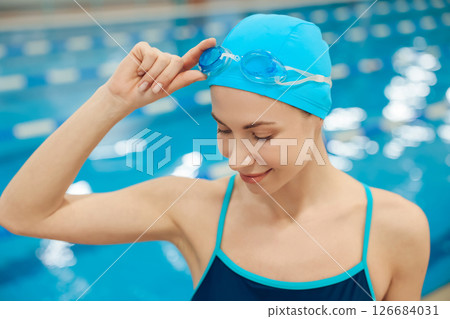 Young woman in swimsuit and swimming cap getting ready to swim in the pool Young woman in swimsuit and swimming cap getting ready to swim in the pool 126684031