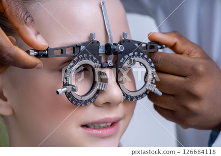 Doctor adjusting optometric tool while testing vision of a girl 126684118